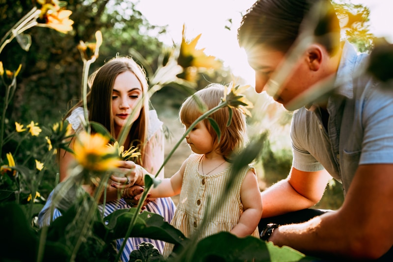 Family Photography, mom and dad examine flowers in a garden with their young daughter