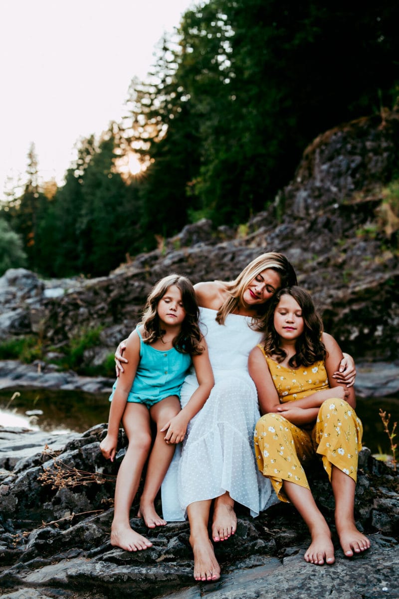 mother and two daughters sitting on rocks embracing with eyes closed