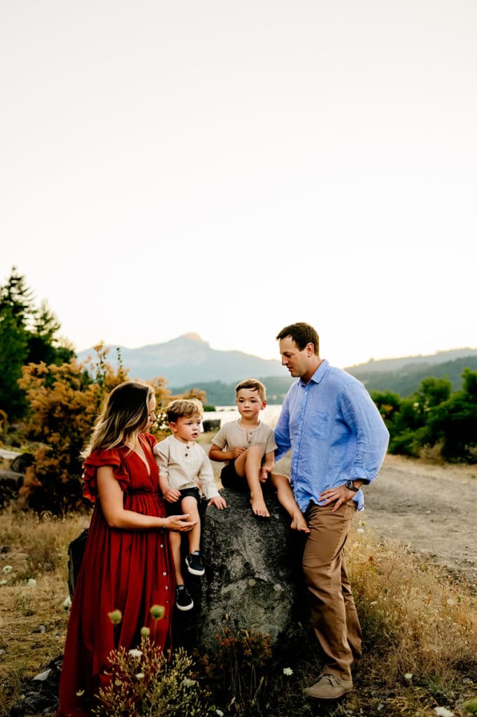 Family Photographer, mom and dad are outside as their two boys sit on a large rock