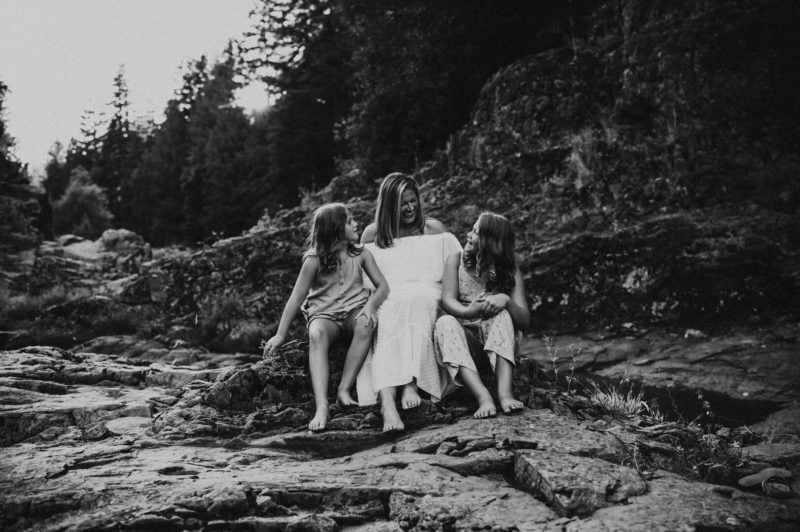 mother and daughters sitting on rocks smiling at each other during family session 