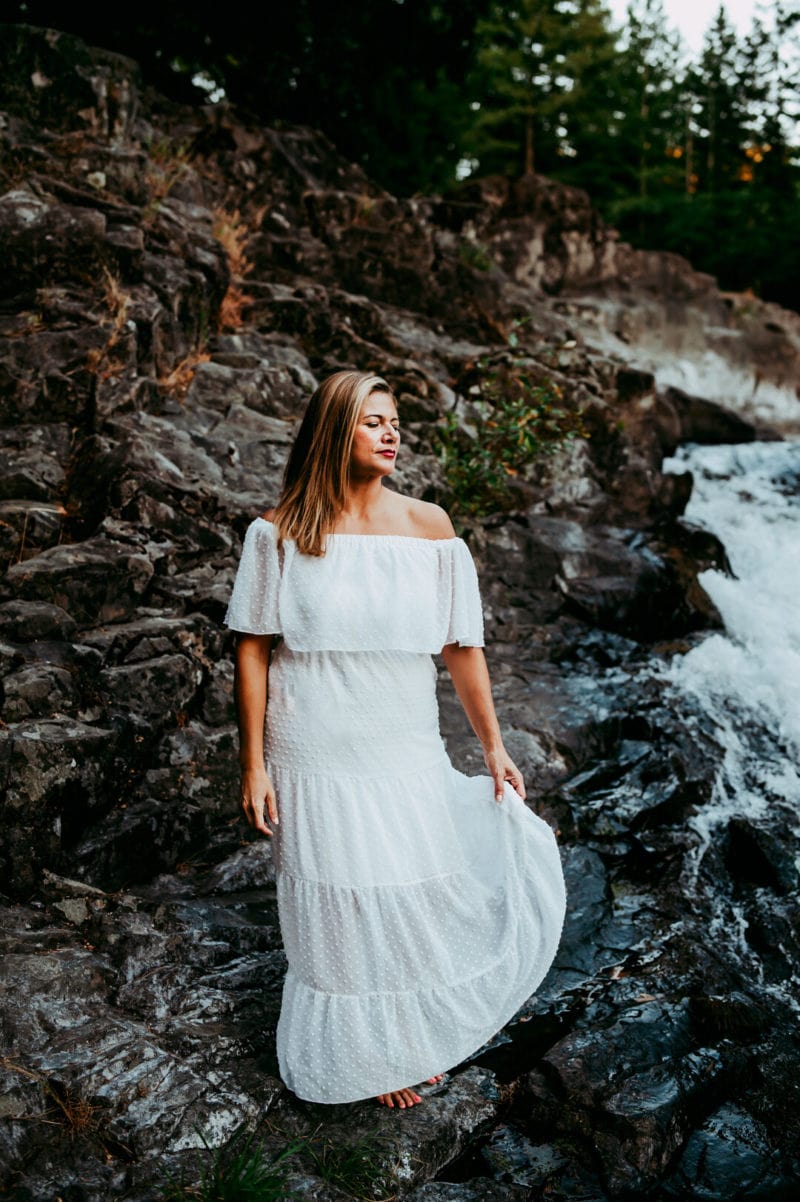 woman in a white dress with eyes closed waterfall on the background