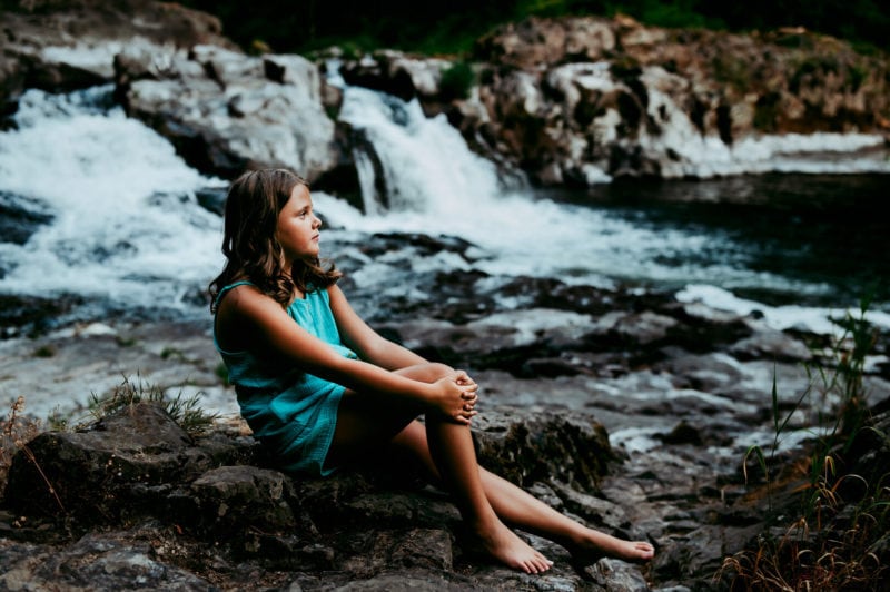 young girl sitting by a waterfall in oregon