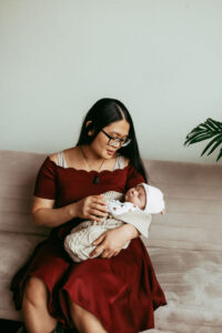 mom holds baby while sitting on a sofa at in home newborn session in Portland OR
