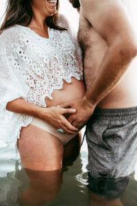 close up of pregnant woman's belly in a lake with her partner holding her belly