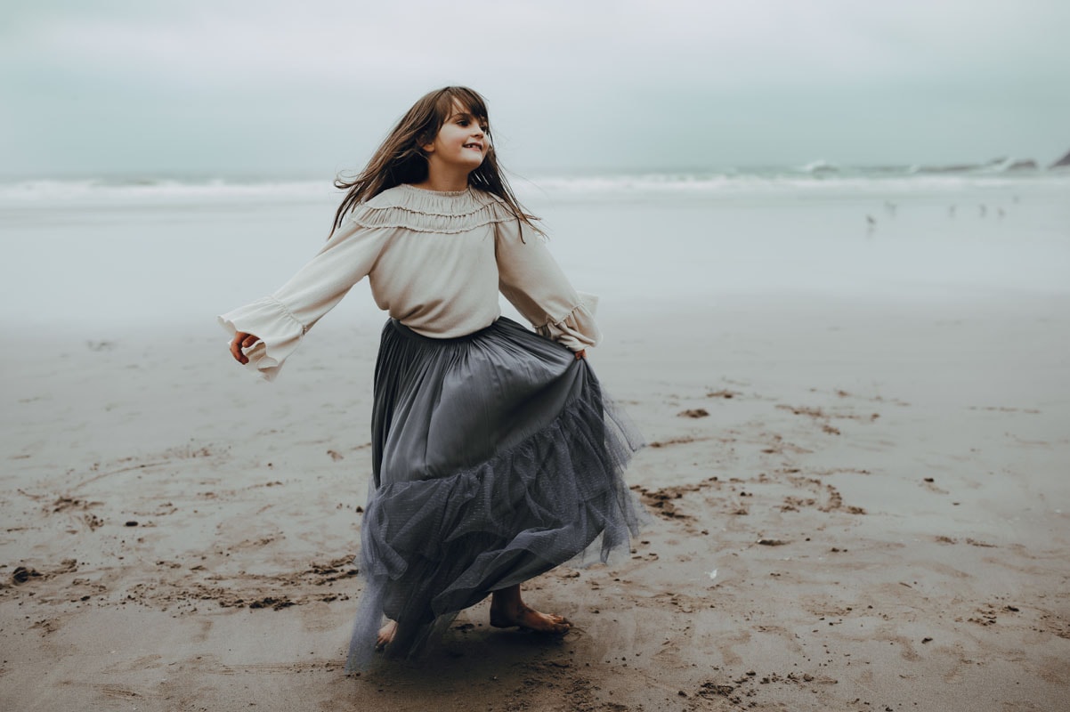 young girl dances during family session at oregon coast