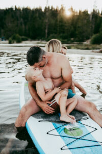 portland motherhood and Family Photographer, a father and son embrace and admire each other on a paddle board in lake waters