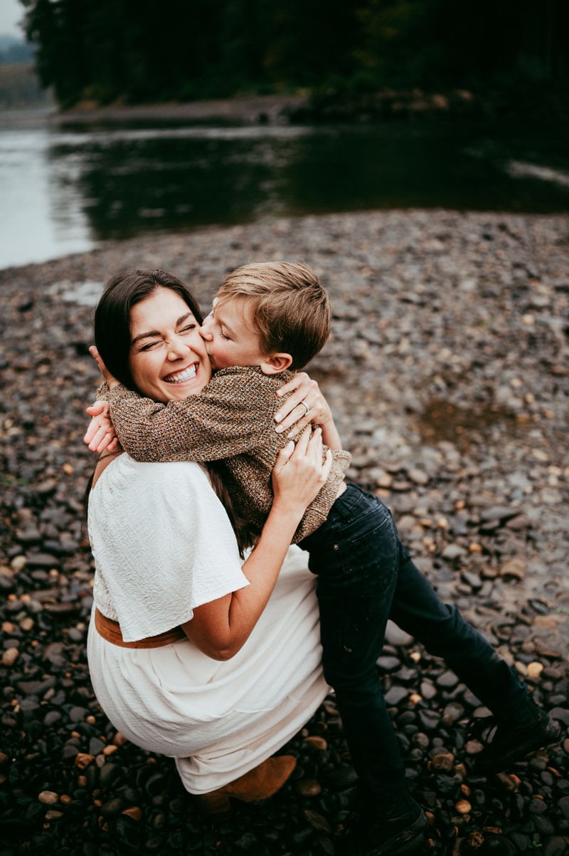 Family Photographer, a young boy kisses his mother next to a quiet river outside