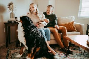 mom plays with dog while holding newborn dad looks on