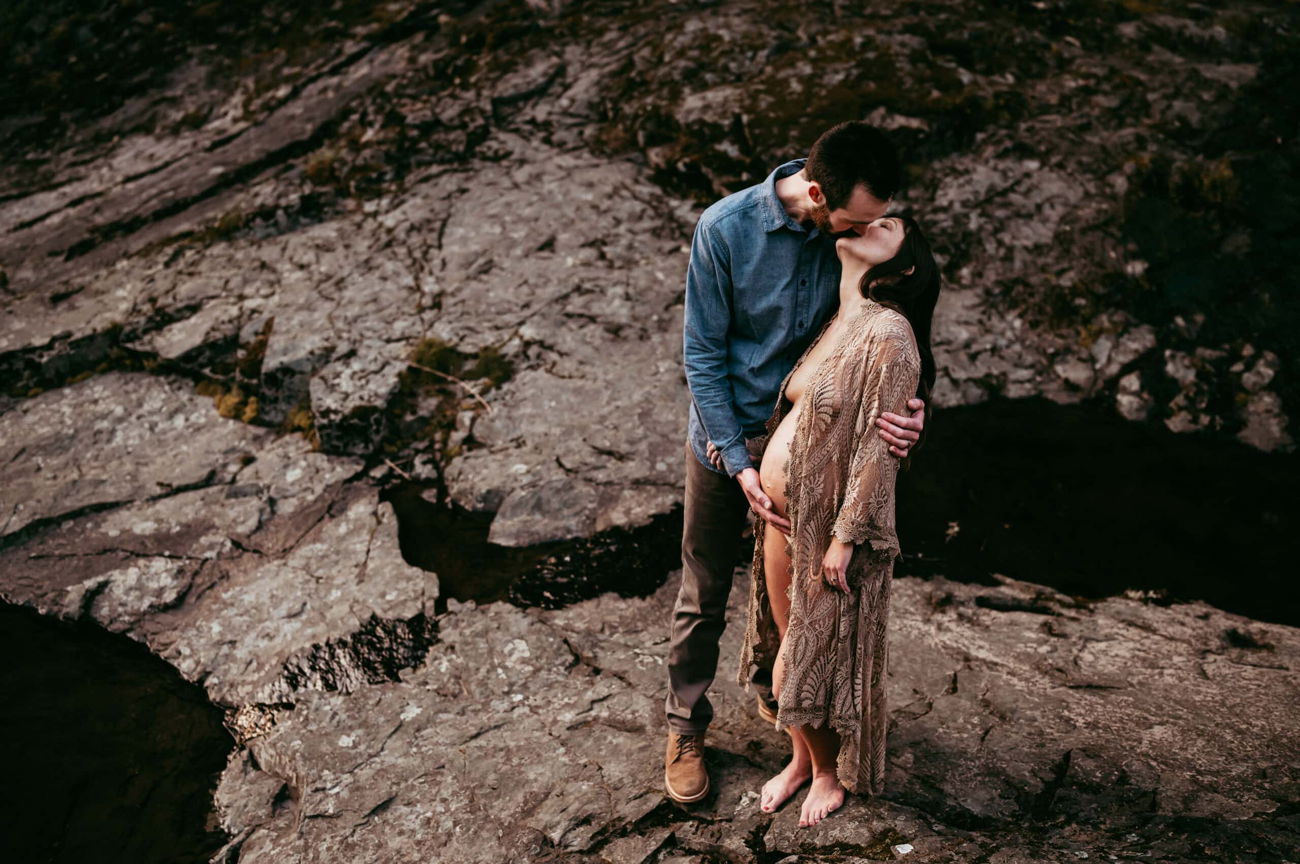Maternity Photographer, a man kisses his expectant wife on large rocks outside