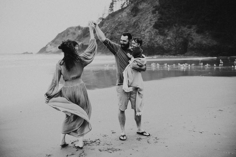mom dad and child dancing during family session in cannon beach