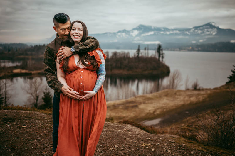 pregnant woman and in a red dress and husband posing at columbia river gorge for maternity session 